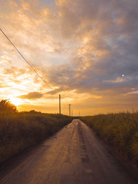 Road amidst field against sky during sunset
