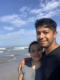 Portrait of smiling man with son at beach against sky