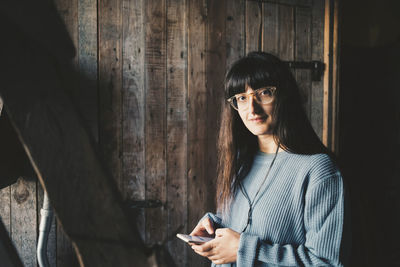 Portrait of smiling woman using smart phone by wooden wall at holiday villa