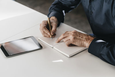 Businessman writing in notebook next to tablet
