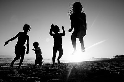 Silhouette children on beach against sky during sunset