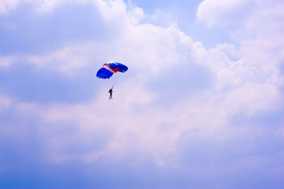 Low angle view of people paragliding against sky