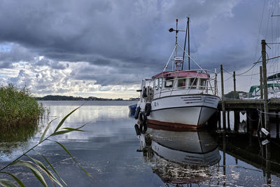 Fishing boats moored at harbor against sky