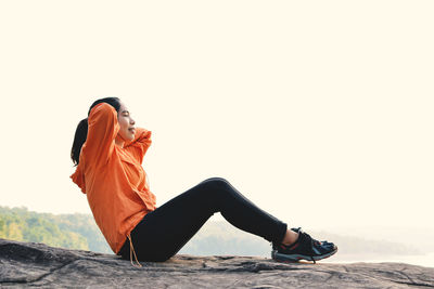 Young woman exercising on cliff against clear sky