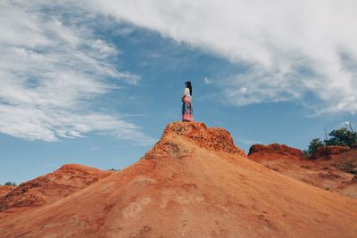 Low angle view of woman standing on rock against sky