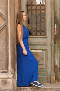 Side view of thoughtful beautiful woman standing on steps by closed weathered doors
