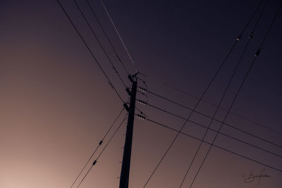 Low angle view of electricity pylon against clear sky during sunset