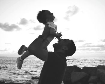 Full length of man and his son standing on beach against sky