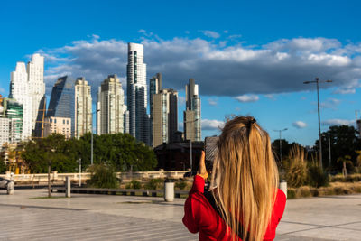 Mature blonde adult woman taking a smartphone photo of a group of buildings in the puerto madero