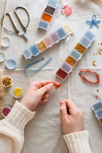 The girl's hands are weaving a beaded bracelet and items for beading on the table. 