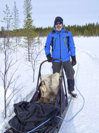 Portrait of man wearing warm clothing holding sled in snow