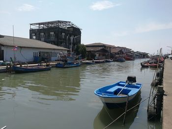 Boats moored in canal by buildings against sky