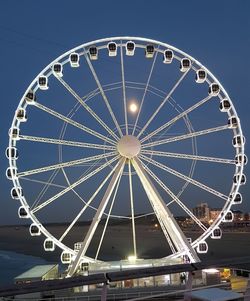 Low angle view of illuminated ferris wheel against blue sky