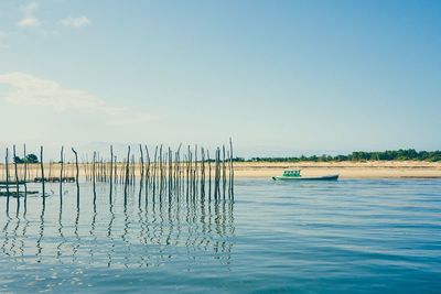 Reflection of wooden post in seascape against blue sky