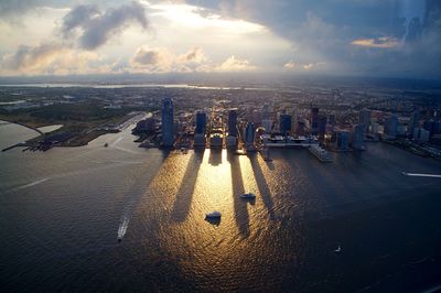 High angle view of cityscape by seashore against cloudy sky