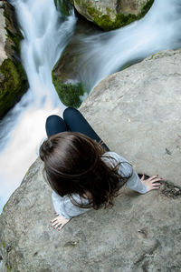 Rear view of young woman sitting by rock formation