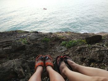 Low section of woman relaxing on rock by sea