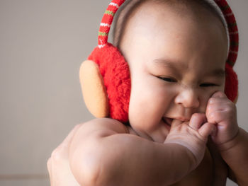 Cropped image of hands holding cute baby boy wearing ear muff against wall