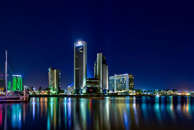 Illuminated buildings by river against sky at night