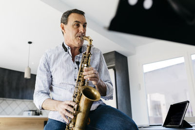 Musician practicing saxophone sitting by tablet pc at home