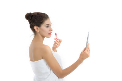 Young woman applying lipstick against white background