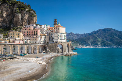 View of houses on mountain by sea against clear blue sky during sunny day