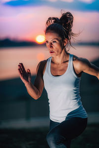 Young woman with arms raised at sunset