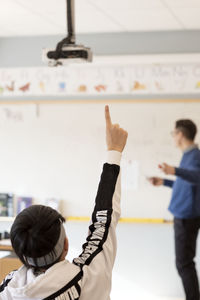 Teenage boy raising hand in classroom