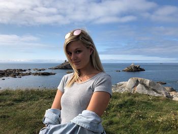 Young woman on rock by sea against sky