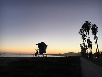 Silhouette lifeguard hut on beach against clear sky at sunset