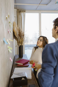 Male and female colleagues discussing over sticky notes on wall in creative office