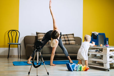 Mother fitness instructor personal trainer record video near camera at home with baby daughter