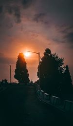 Silhouette trees by road against sky during sunset