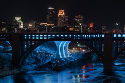 Illuminated bridge over river by buildings in city at night