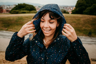 Smiling young woman with raincoat against field