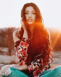 Portrait of young woman sitting on field during sunset