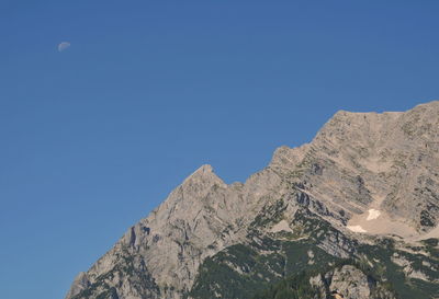 Low angle view of rocky mountain against clear blue sky