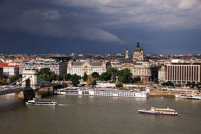 Boats in river by buildings in city against sky