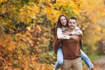 Portrait of young woman with autumn leaves against trees