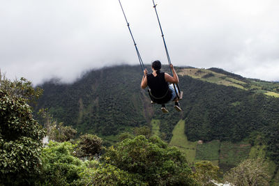 Rear view of woman playing on swing against sky