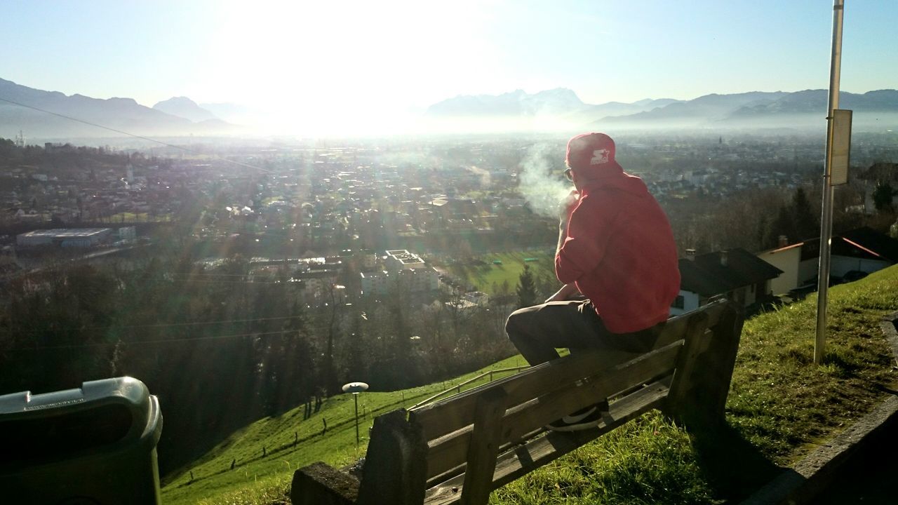 lifestyles, leisure activity, sunlight, sun, sunbeam, men, casual clothing, nature, sitting, landscape, field, mountain, lens flare, grass, sky, water, outdoors, rear view