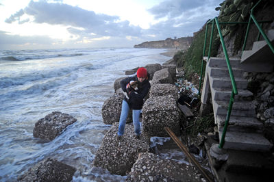 Man standing on rocks at beach against sky