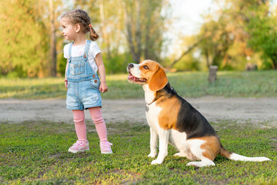 Full length of girl standing by dog in park