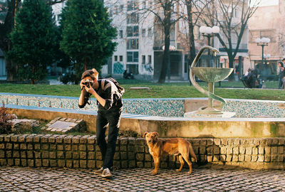 Man photographing with camera while standing by dog on street