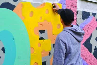 Rear view of man spray painting graffiti on wall