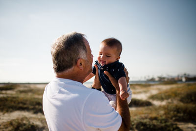 Grandfather holding grandson while standing on beach