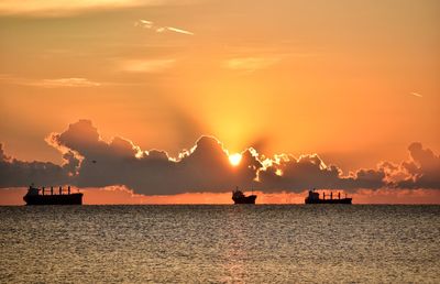 Silhouette boats in sea against cloudy sky during sunset