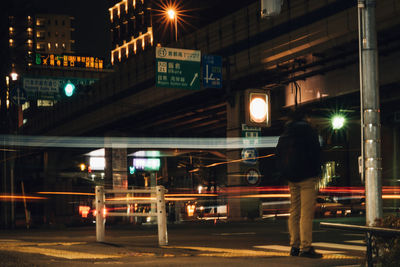 Rear view of man standing on illuminated street at night