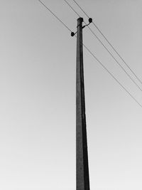 Low angle view of power lines with pole against clear sky