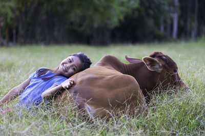 Portrait of cute girl sitting by cow on field